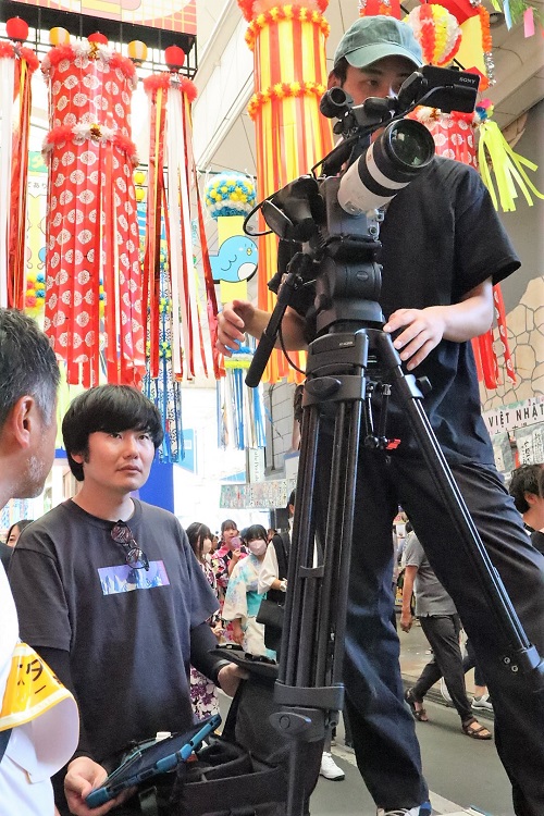 商店街の七夕祭りの様子を撮影中。左:西川達郎監督